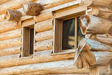 Primo piano della facciata in legno di una casa di tronchi ad Amden, in Svizzera, con una vista dettagliata di due finestre in legno EgoWoodstar perfettamente integrate nella massiccia costruzione in tronchi.